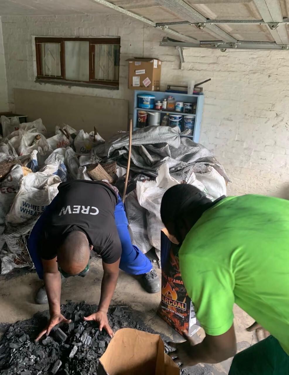 Worker bending over, bagging charcoal